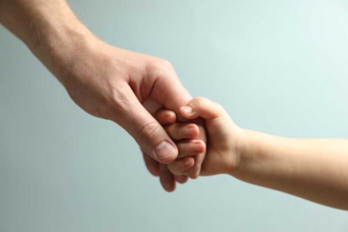 Father,And,Child,Holding,Hands,On,Light,Blue,Background,,Closeup