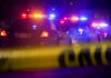 Police cars with flashing lights at a nighttime scene behind crime scene tape
