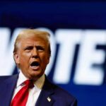 A man passionately speaking at a campaign event with a VOTE backdrop