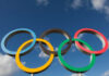 Five interlocking Olympic rings against a blue sky with clouds