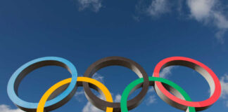 Five interlocking Olympic rings against a blue sky with clouds