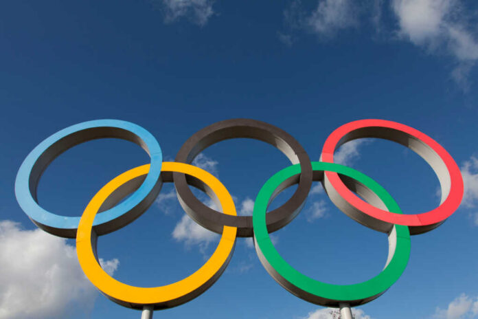 Five interlocking Olympic rings against a blue sky with clouds