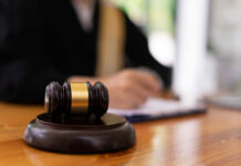 A gavel on a wooden table with a blurred figure of a person in professional attire in the background