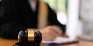 A gavel on a wooden table with a blurred figure of a person in professional attire in the background