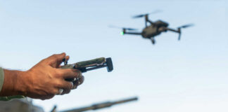 Person controlling a drone with a remote while a tank is in the background