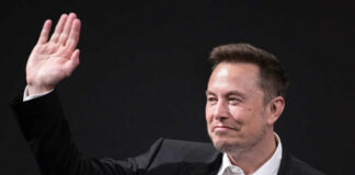 A man in a suit waving with a smile during a conference