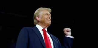 A man in a suit with a red tie raising his fist confidently during a speech