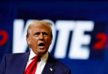 A man passionately speaking at a campaign event with a VOTE backdrop