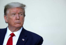 A serious-looking man in formal attire with an American flag pin
