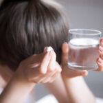 Person holding a pill and a glass of water, appearing distressed