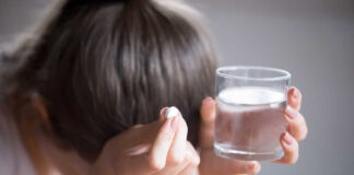 Person holding a pill and a glass of water, appearing distressed