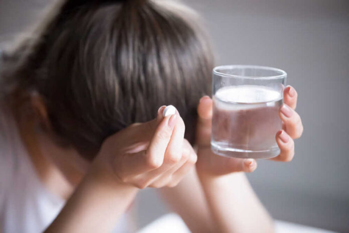 Person holding a pill and a glass of water, appearing distressed