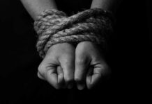 Close-up of two hands tightly bound with rope against a dark background