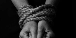 Close-up of two hands tightly bound with rope against a dark background
