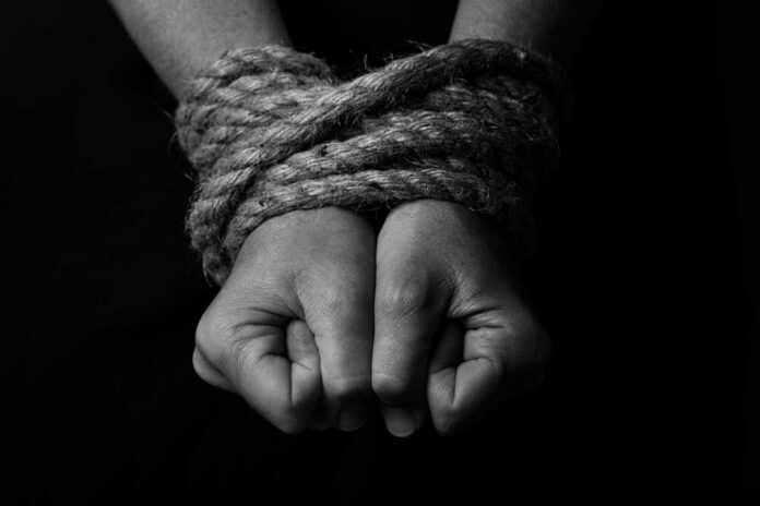 Close-up of two hands tightly bound with rope against a dark background