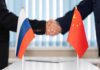 Handshake between two individuals with Russian and Chinese flags in the foreground