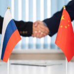 Handshake between two individuals with Russian and Chinese flags in the foreground