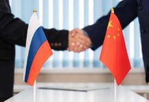 Handshake between two individuals with Russian and Chinese flags in the foreground