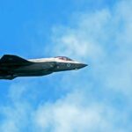 Fighter jet flying against a blue sky with clouds