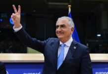 A man in a suit making a peace sign gesture at a podium