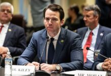 A man in a suit sitting at a table during a government hearing