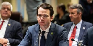 A man in a suit sitting at a table during a government hearing