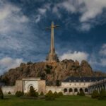 A large cross atop a rocky hill with a building in the foreground
