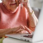 Elderly woman on a phone call while using a laptop