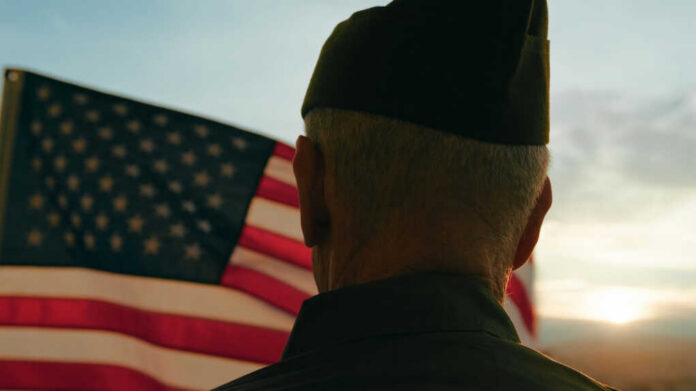 A veteran in uniform standing in front of an American flag during sunset