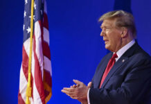 Trump’s Immigration Policy Faces Fierce Senate Challenge A man in a suit standing beside an American flag during a public speaking event