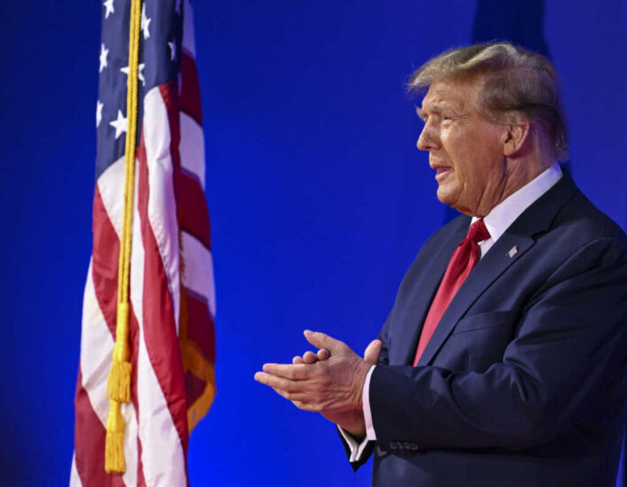 A man in a suit standing beside an American flag during a public speaking event