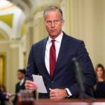 A male politician in a suit holding a notepad in a government building