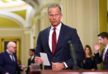 Democrats Accused: “Holding Government Hostage” A male politician in a suit holding a notepad in a government building