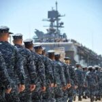 Uniformed naval personnel marching towards a ship