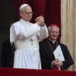 A religious leader in white robes gestures during a public address
