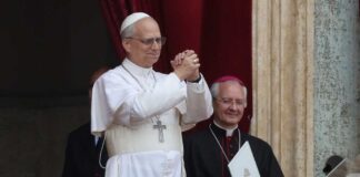 A religious leader in white robes gestures during a public address