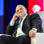 A speaker sitting on a stage with a thoughtful expression at a political conference