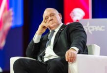 A speaker sitting on a stage with a thoughtful expression at a political conference