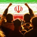 Crowd of people raising their fists in front of the Iranian flag