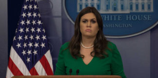 A government official at a press briefing in front of the American flag
