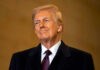 A man in formal attire smiling confidently against a neutral background