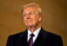 A man in formal attire smiling confidently against a neutral background