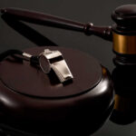 A silver whistle and a gavel on a reflective surface