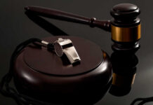 A silver whistle and a gavel on a reflective surface