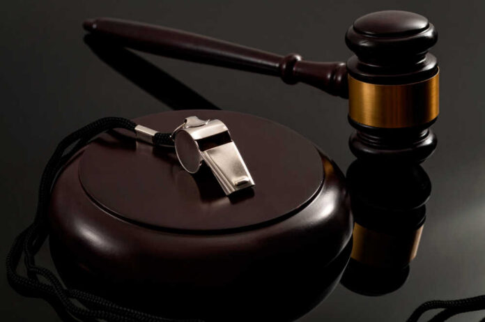 A silver whistle and a gavel on a reflective surface