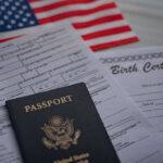 A passport and birth certificate on a table with an American flag in the background
