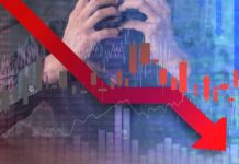 A stressed businessman holding his head with a downward stock market graph in the background