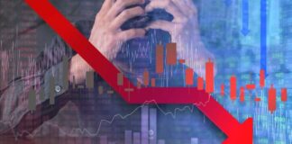 A stressed businessman holding his head with a downward stock market graph in the background