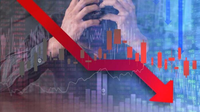 A stressed businessman holding his head with a downward stock market graph in the background