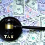 A gavel with the word 'TAX' on it placed on a background of US dollar bills